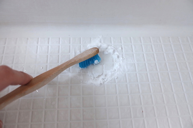 床の汚れに重曹の粉をふりかけ、濡らした歯ブラシでペースト状にして擦っている様子